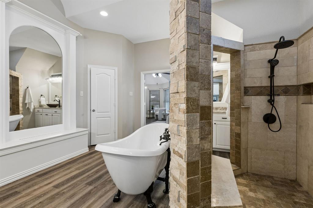 317 Singing Quail Trail Haslet, TX 76052 - Photo 17 of 32 Clawfoot soaking tub, wood-finish flooring, stone-clad partition, and a walk-in shower with tile surround and dark bronze fixtures