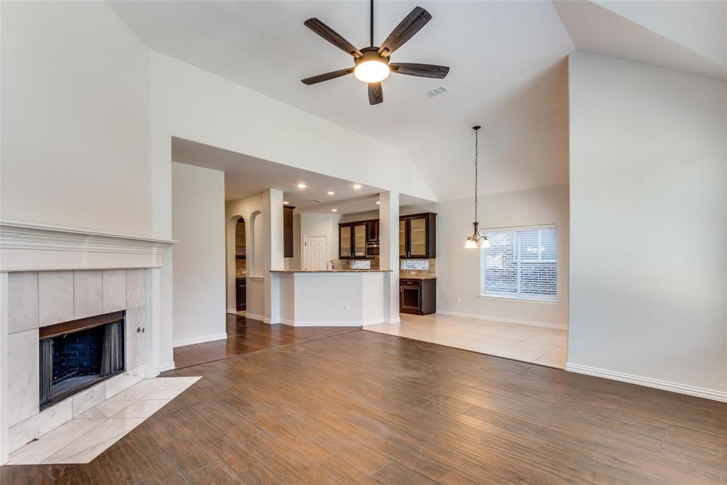 2344 Ranchview Drive Little Elm, TX 75068 - Photo 4 of 24 Spacious living area featuring wood-finish flooring, a tiled fireplace with mantel, and a vaulted ceiling with a ceiling fan
