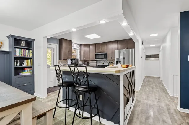 a kitchen with stainless steel appliances kitchen island granite countertop a table chairs refrigerator and a stove