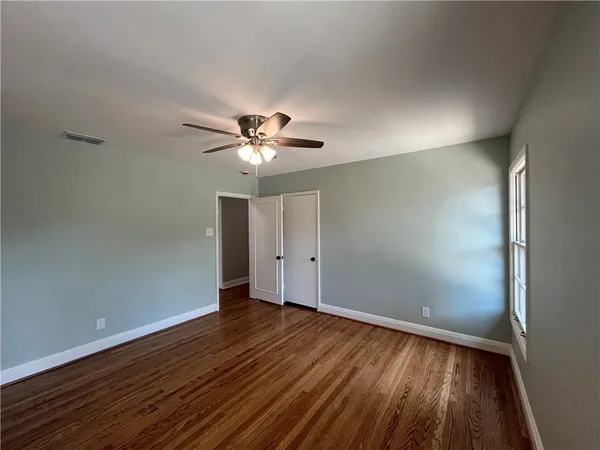 an empty room with wooden floor chandelier fan and windows