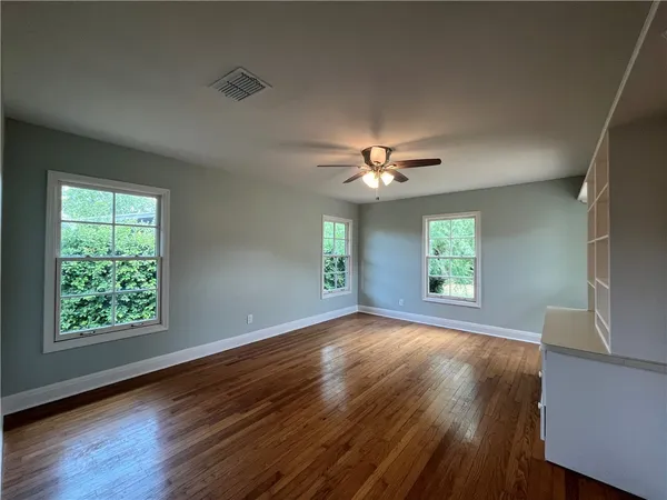 an empty room with wooden floor chandelier fan and windows