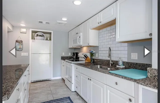 a kitchen with granite countertop a refrigerator a sink and white cabinets