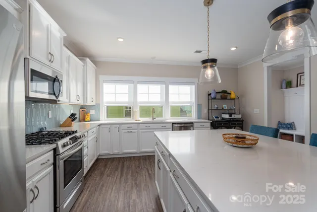 a kitchen with stainless steel appliances a stove a sink dishwasher a microwave oven and a dining table with wooden floor