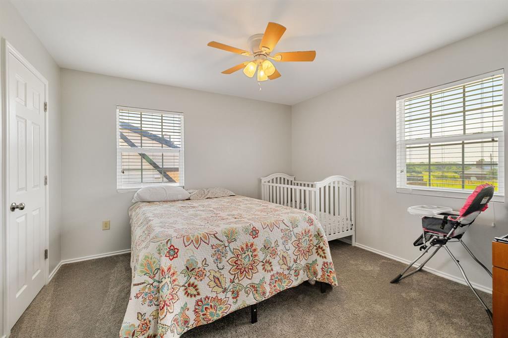 12240 Wellington Road Ponder, TX 76259 - Photo 34 of 40 Carpeted interior room featuring light gray walls, two windows with horizontal blinds, a white paneled door, and a ceiling fan with light fixture