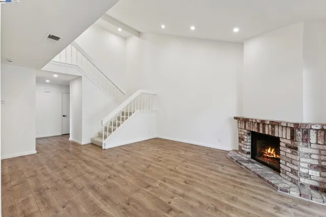 a view of an empty room with wooden floor fireplace and a window