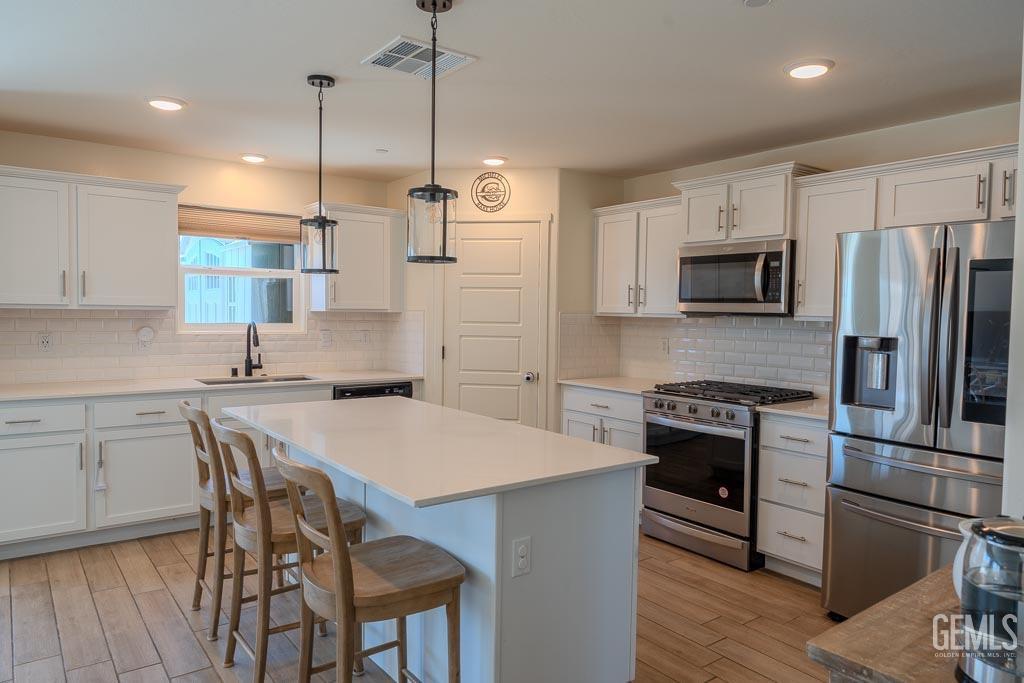Undisclosed Address Bakersfield, CA 93311 - Photo 11 of 24 a kitchen with kitchen island a stove a refrigerator a sink and a wooden floor
