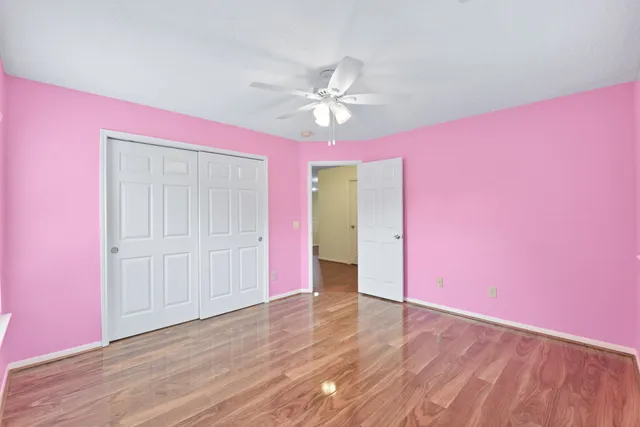 a view of an empty room with wooden floor and a ceiling fan