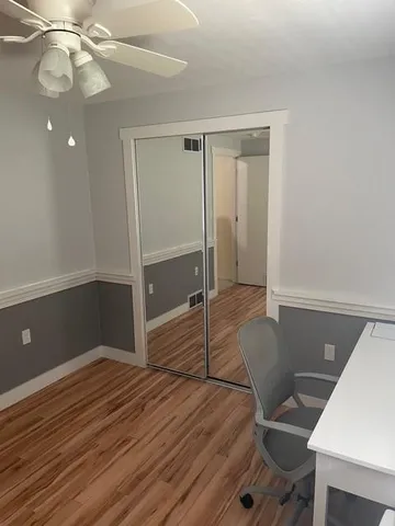 a view of an empty room with wooden floor and a ceiling fan