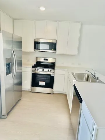 a kitchen with stainless steel appliances white cabinets a sink a stove a microwave and a refrigerator