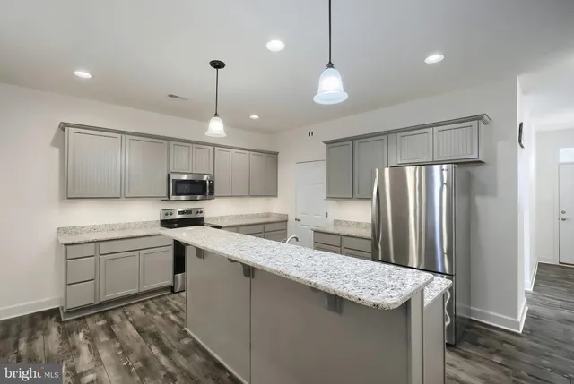 a kitchen with stainless steel appliances granite countertop a sink a stove a refrigerator and island with wooden floor
