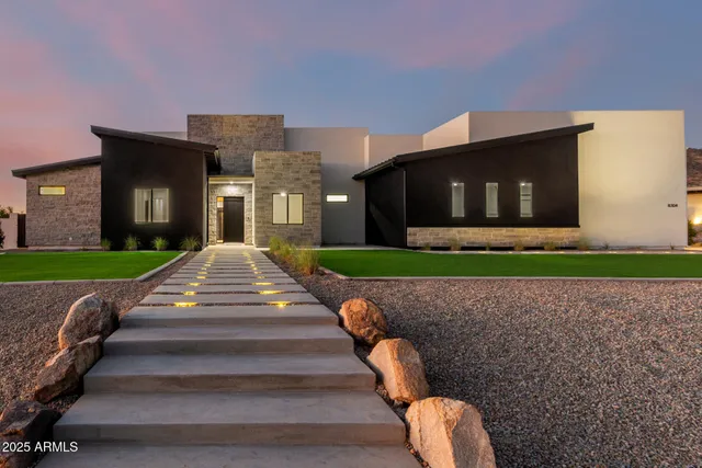 a front view of a house with large trees and cars parked
