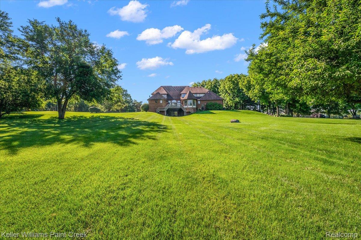 69069 Campground Road Romeo, MI 48065 - Photo 11 of 78 Expansive green lawn with mature trees and a brick-sided residence featuring multiple windows and a rear deck
