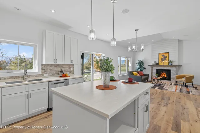 a kitchen with stainless steel appliances a stove a sink a oven a dining table and chairs with wooden floor