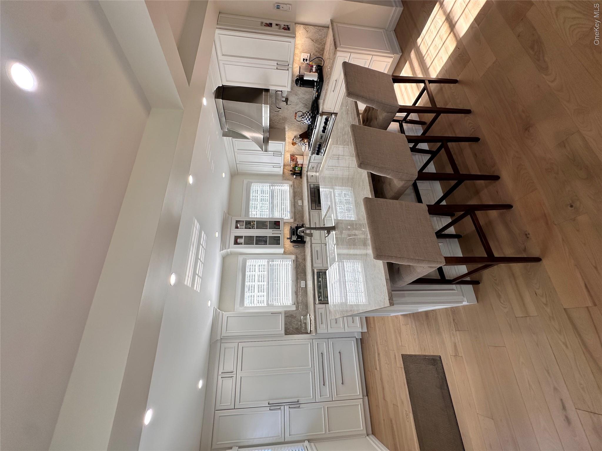 252 Beverly Road Queens, NY 11363 - Photo 3 of 19 Kitchen featuring light-toned wood-finish flooring, white cabinetry, a large center island with a light-colored countertop, and a stainless steel range hood