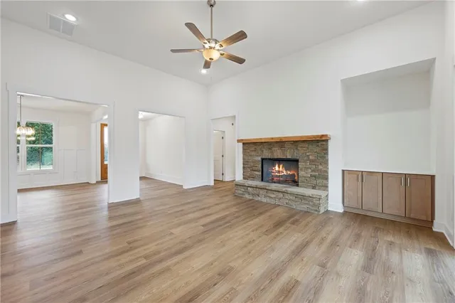 an empty room with wooden floor a ceiling fan a fireplace and windows