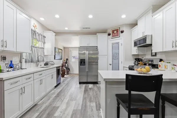 a kitchen with stainless steel appliances kitchen island granite countertop a refrigerator a stove a sink a dining table and chairs with wooden floor
