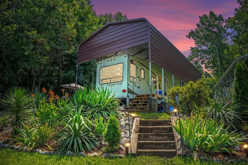 This tranquil outdoor retreat features lush greenery and a charming recreational vehicle under a protective cover.