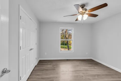 an empty room with wooden floor fan and windows