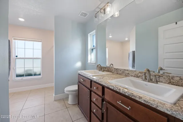 a bathroom with a granite countertop sink a toilet a mirror and a window