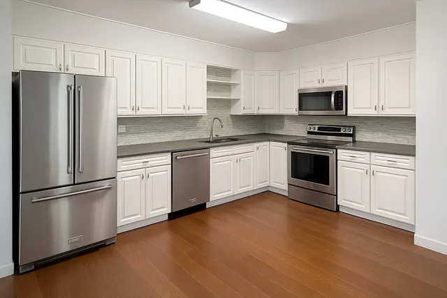 a kitchen with stainless steel appliances granite countertop a refrigerator stove a sink and white cabinets