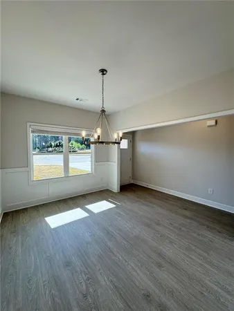an empty room with wooden floor chandelier and windows