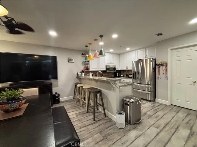 a living room with stainless steel appliances furniture a flat screen tv and a kitchen view