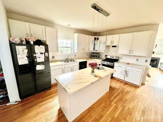 a kitchen with stainless steel appliances a stove a refrigerator a sink a oven and white cabinets with wooden floor