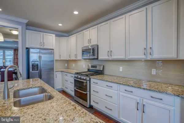 a kitchen with stainless steel appliances granite countertop a stove top oven a refrigerator a sink and white cabinets with wooden floor