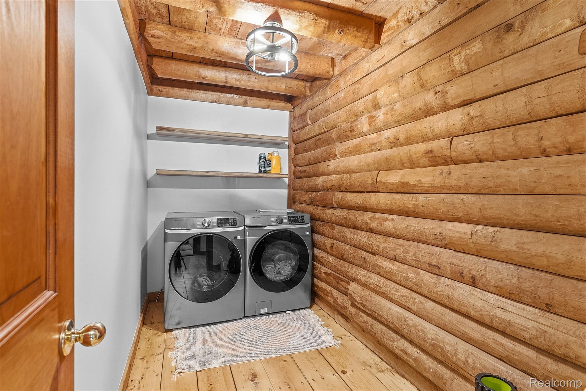 3656 Stanley Road Columbiaville, MI 48421 - Photo 18 of 65 Laundry area featuring a log wall, wood-finish flooring, two floating shelves, and a modern ceiling light fixture