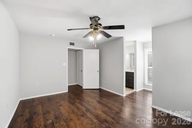 a view of an empty room with wooden floor and a ceiling fan