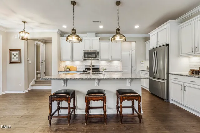 a kitchen with stainless steel appliances granite countertop a dining table chairs refrigerator and sink