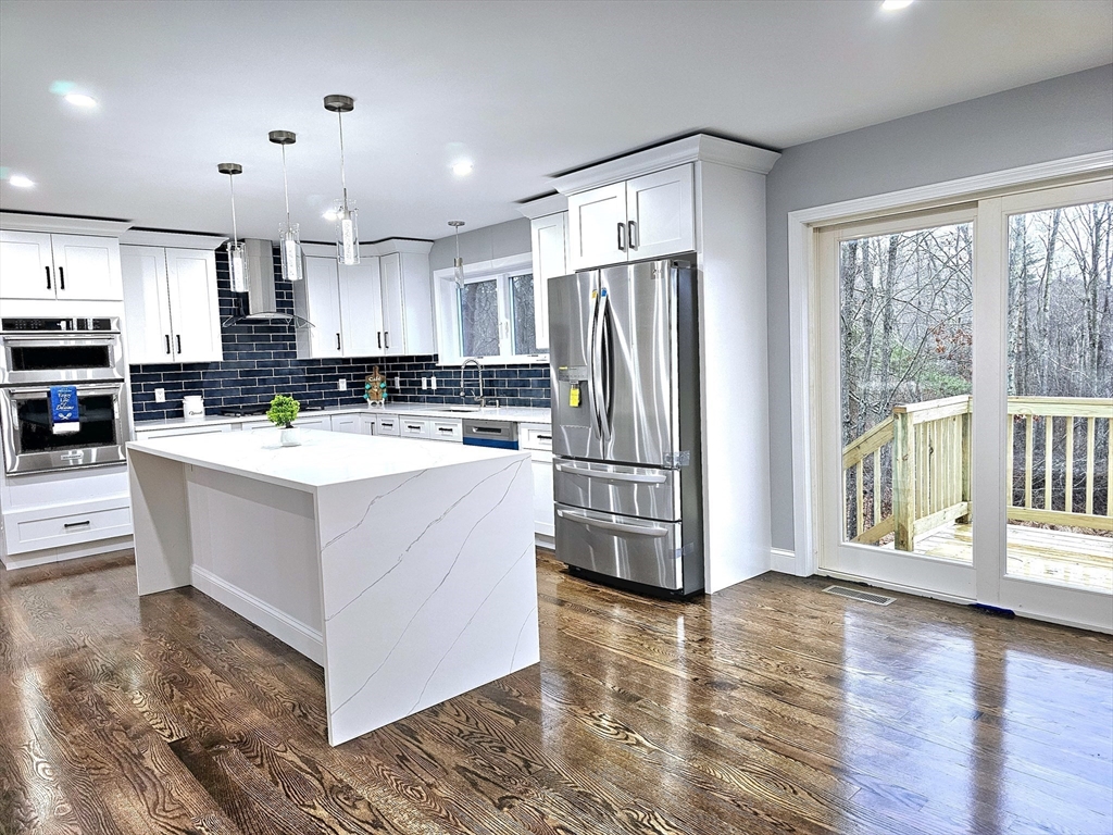 a view of kitchen with stainless steel appliances granite countertop a stove top oven a refrigerator and a view of living room