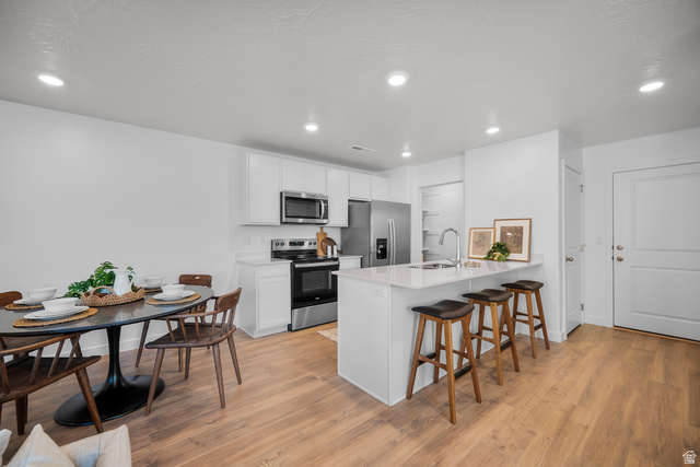 2202 Wolverine Way, Unit 2529 Washington, UT 84780 - Photo 5 of 27 Open-concept kitchen featuring an island with counter seating, stainless steel appliances, white cabinetry, and wood-finish flooring
