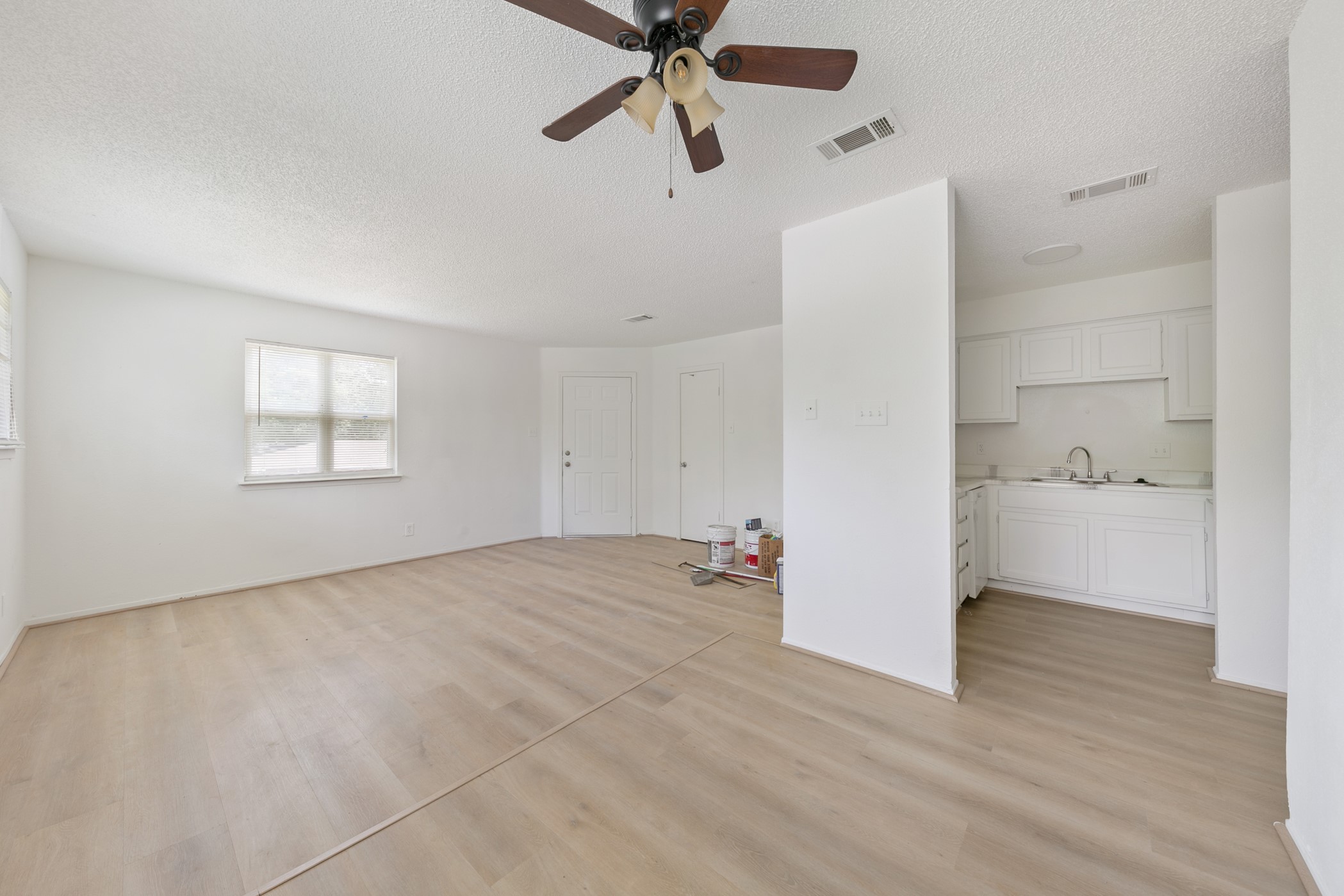700 Lyle W Avenue, Unit D Cleveland, TX 77327 - Photo 10 of 16 This bright, open-concept living area features light wood flooring, a ceiling fan, and ample natural light. Adjacent is a compact kitchen with white cabinetry, offering a clean and modern feel.
