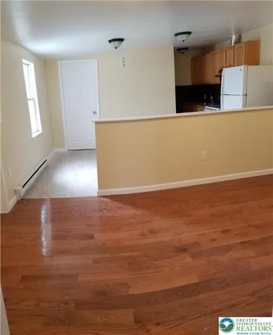 a view of kitchen and empty room with wooden floor