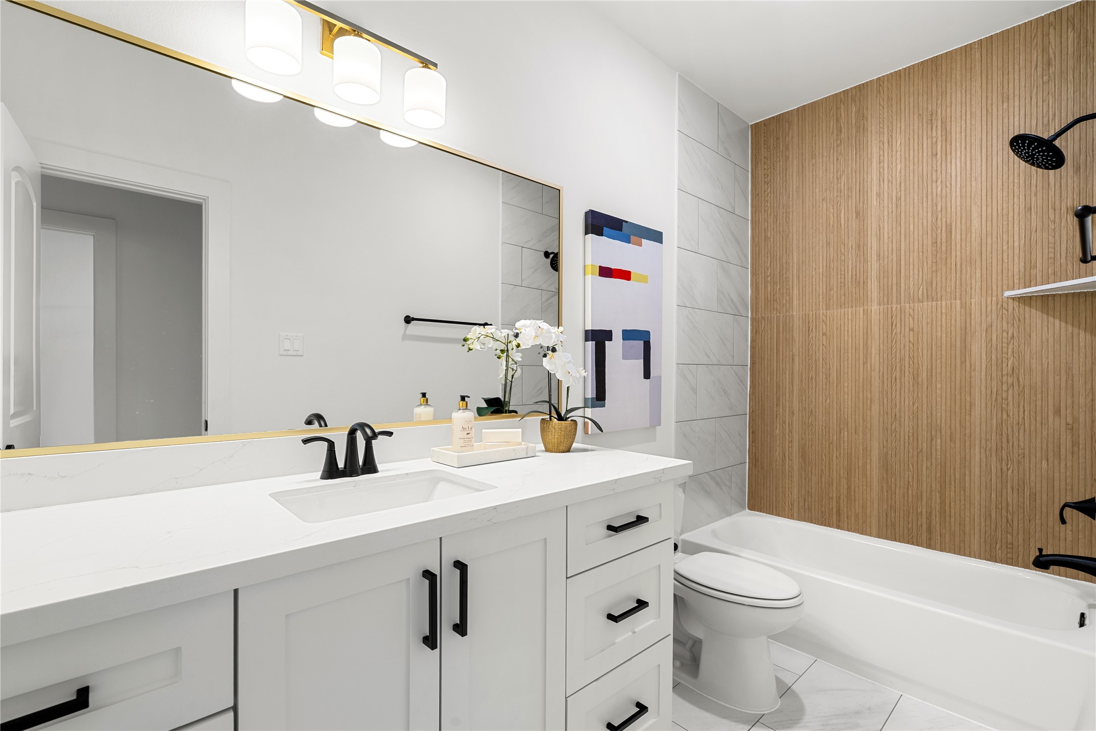 1614 Ojeman Road, Unit I Houston, TX 77055 - Photo 9 of 49 First floor bathroom features a sleek white vanity with black fixtures, a large mirror with stylish lighting, and a bathtub with a wood-accented wall.