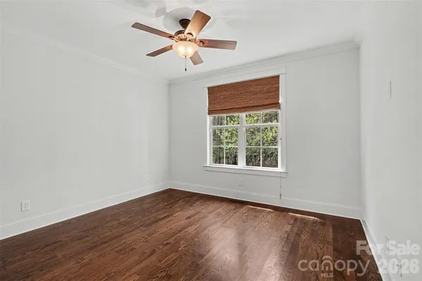 an empty room with wooden floor ceiling fan and window