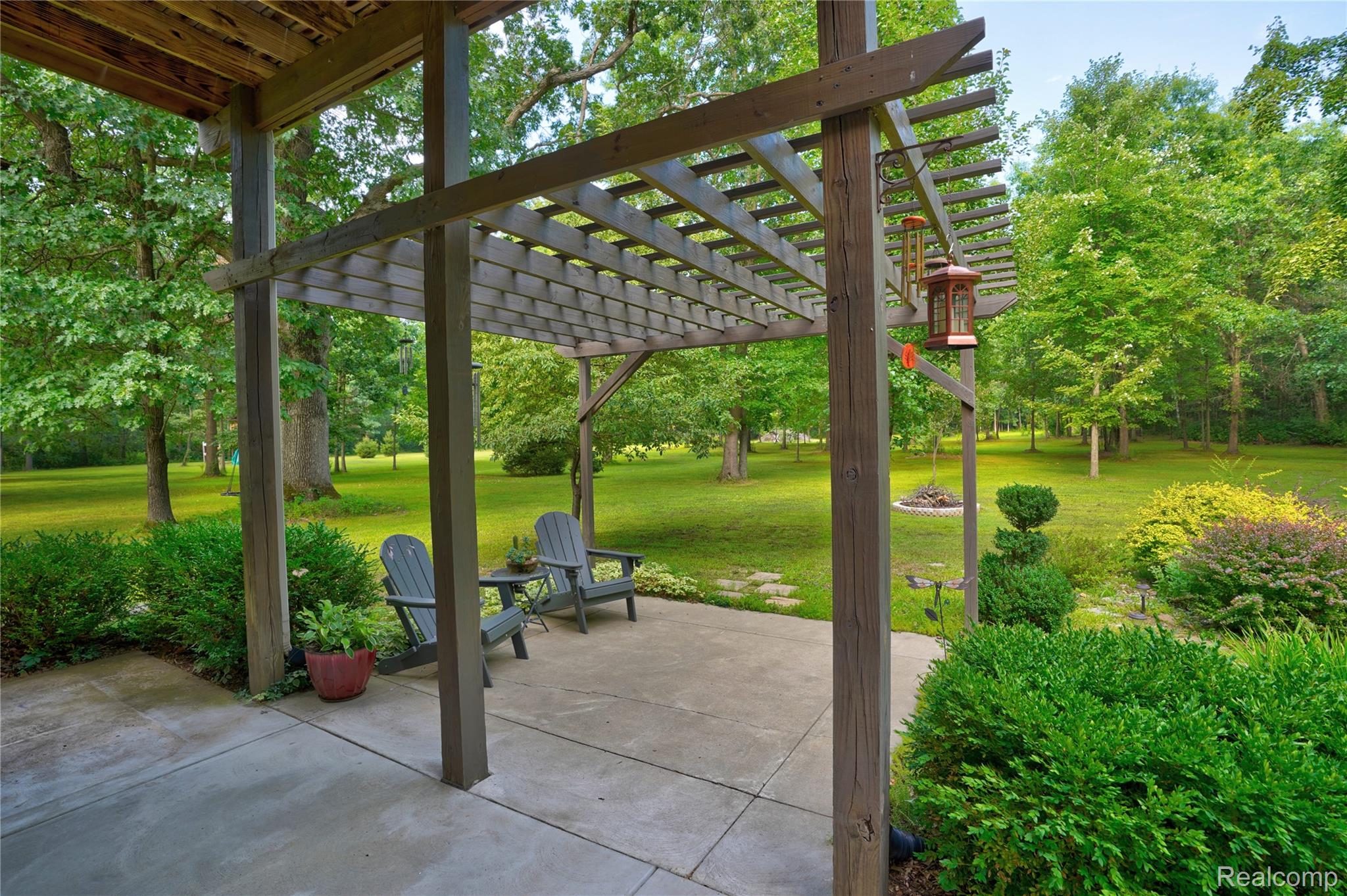 15055 South Duffield Road Byron, MI 48418 - Photo 44 of 61 Expansive patio featuring a wooden pergola, concrete surfacing, and surrounding mature landscaping