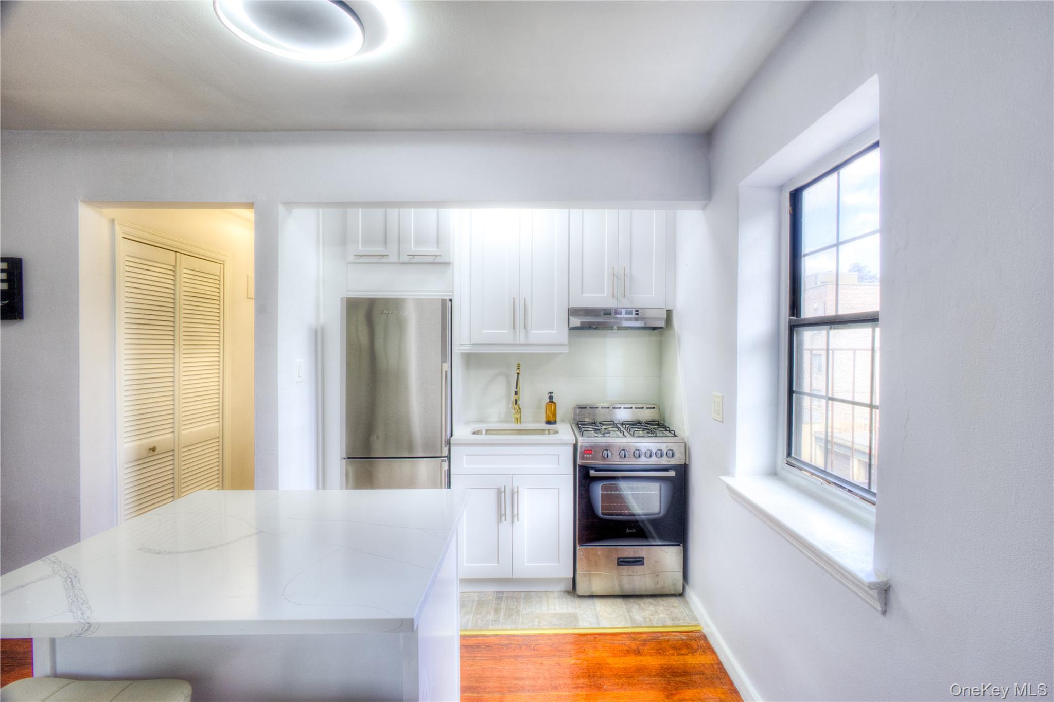 14401 78th Road, Unit 2B Queens, NY 11367 - Photo 13 of 29 Kitchen featuring appliances with stainless steel finishes, white cabinets, light wood-style floors, and under cabinet range hood