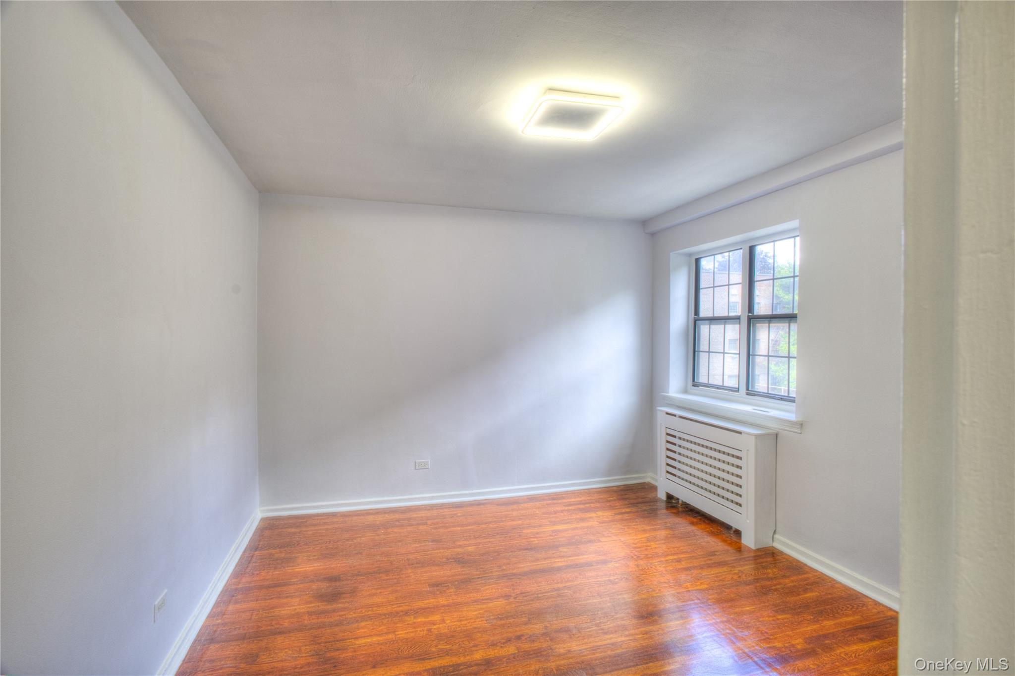 14401 78th Road, Unit 2B Queens, NY 11367 - Photo 15 of 29 Empty room with radiator heating unit and wood finished floors