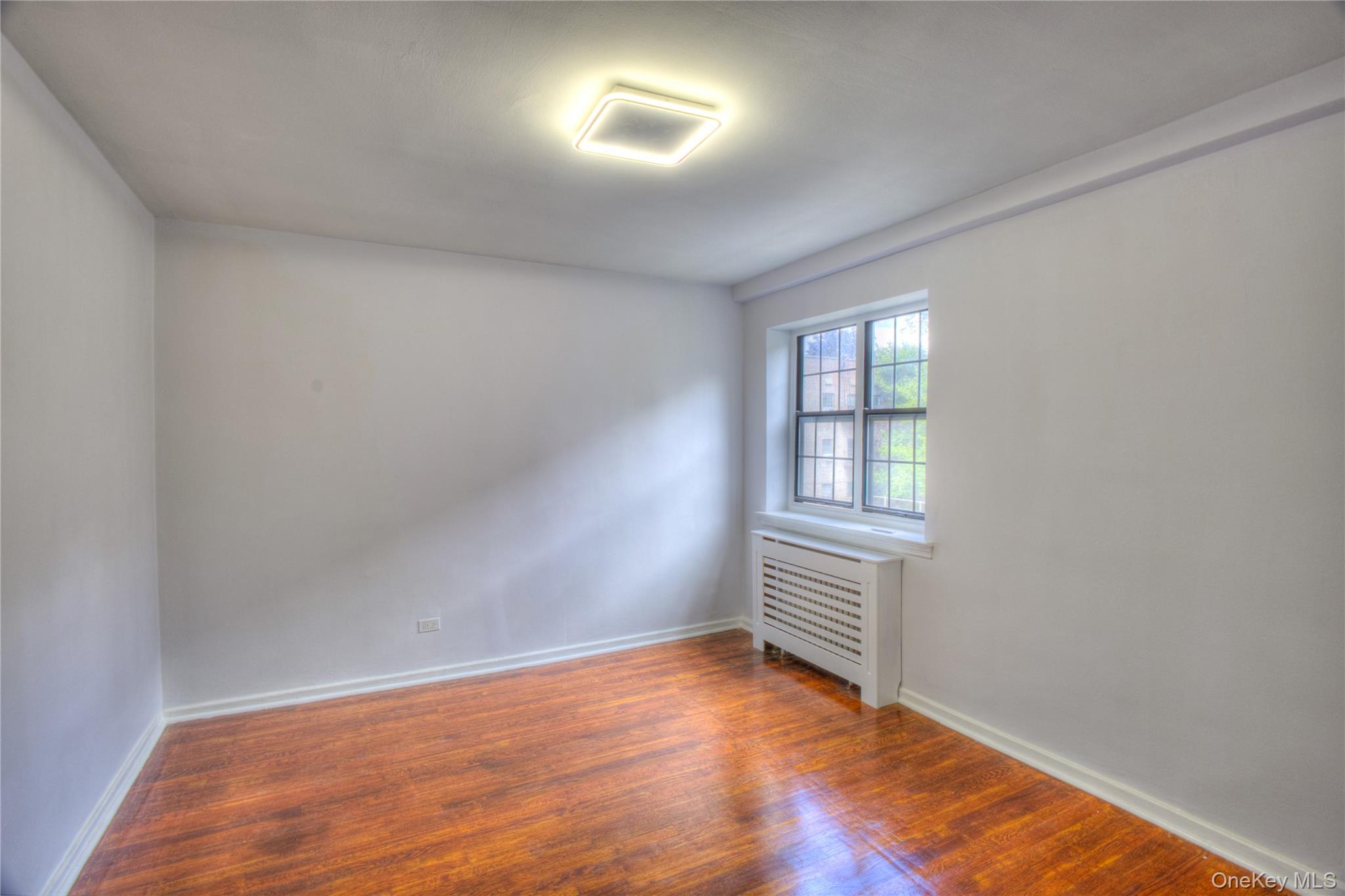 14401 78th Road, Unit 2B Queens, NY 11367 - Photo 16 of 29 Empty room with radiator and wood finished floors