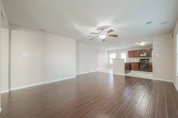 a view of empty room with wooden floor and kitchen view