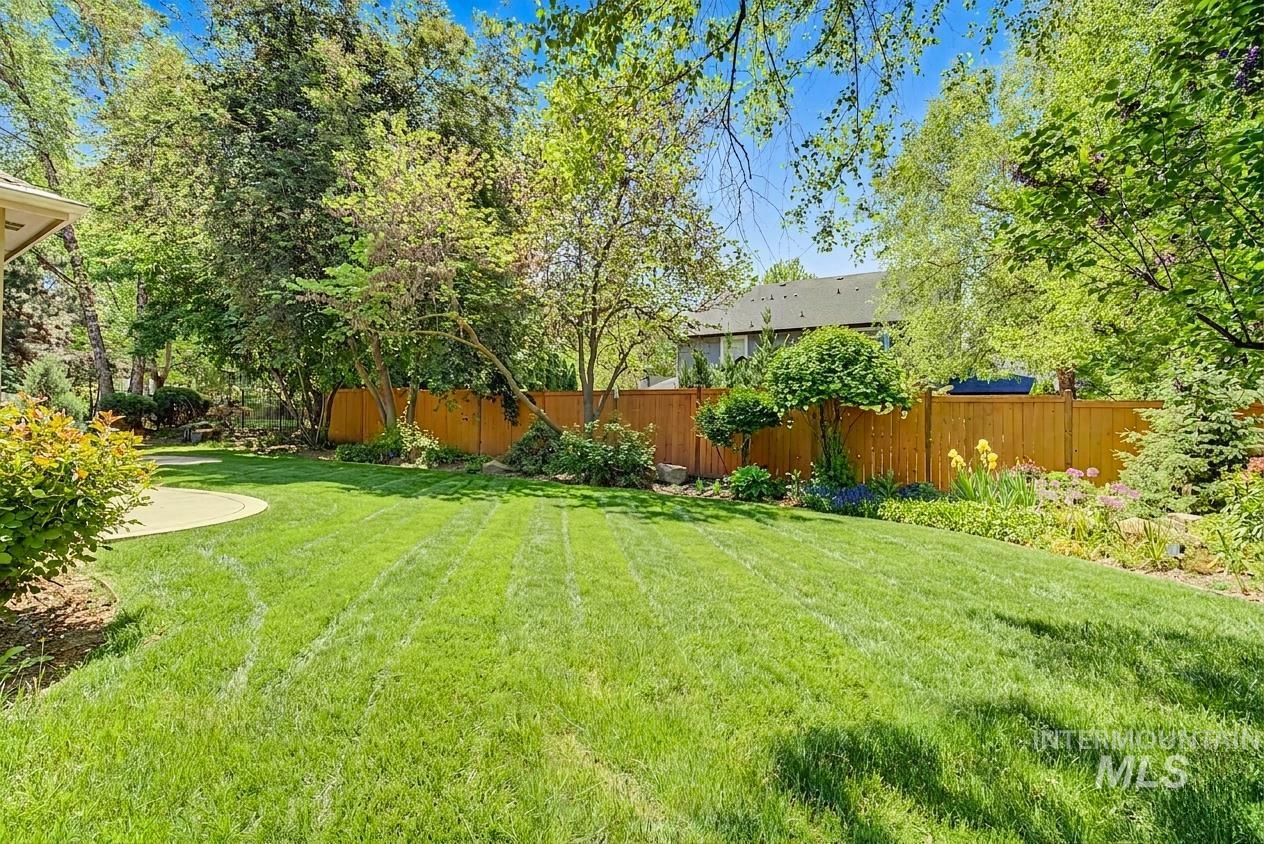 1579 North Watson Way Eagle, ID 83616 - Photo 24 of 30 Expansive green lawn surrounded by mature trees, a wood privacy fence, and integrated garden beds