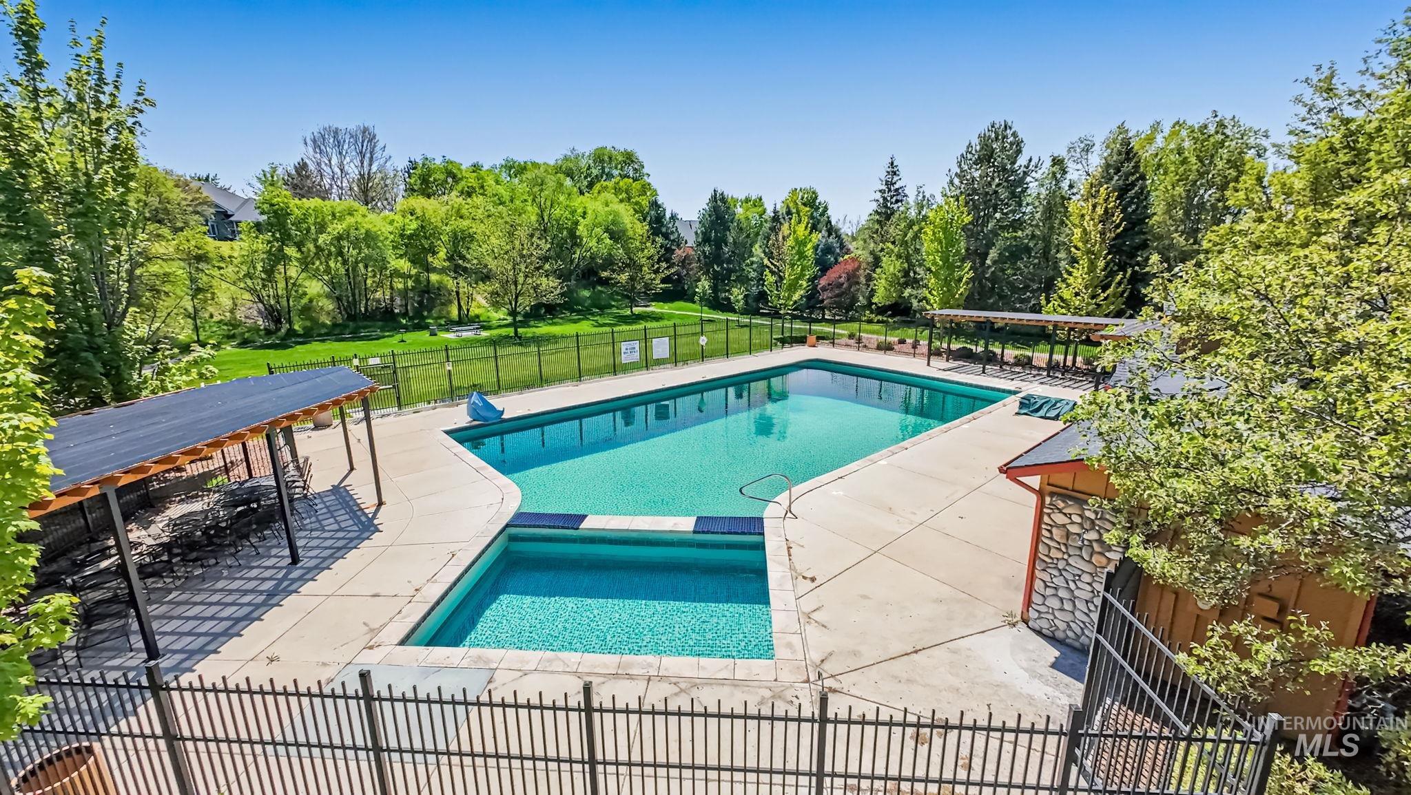 1579 North Watson Way Eagle, ID 83616 - Photo 28 of 30 Fenced swimming pool area featuring a large main pool, a smaller secondary pool, expansive concrete decking, and two distinct shaded structures