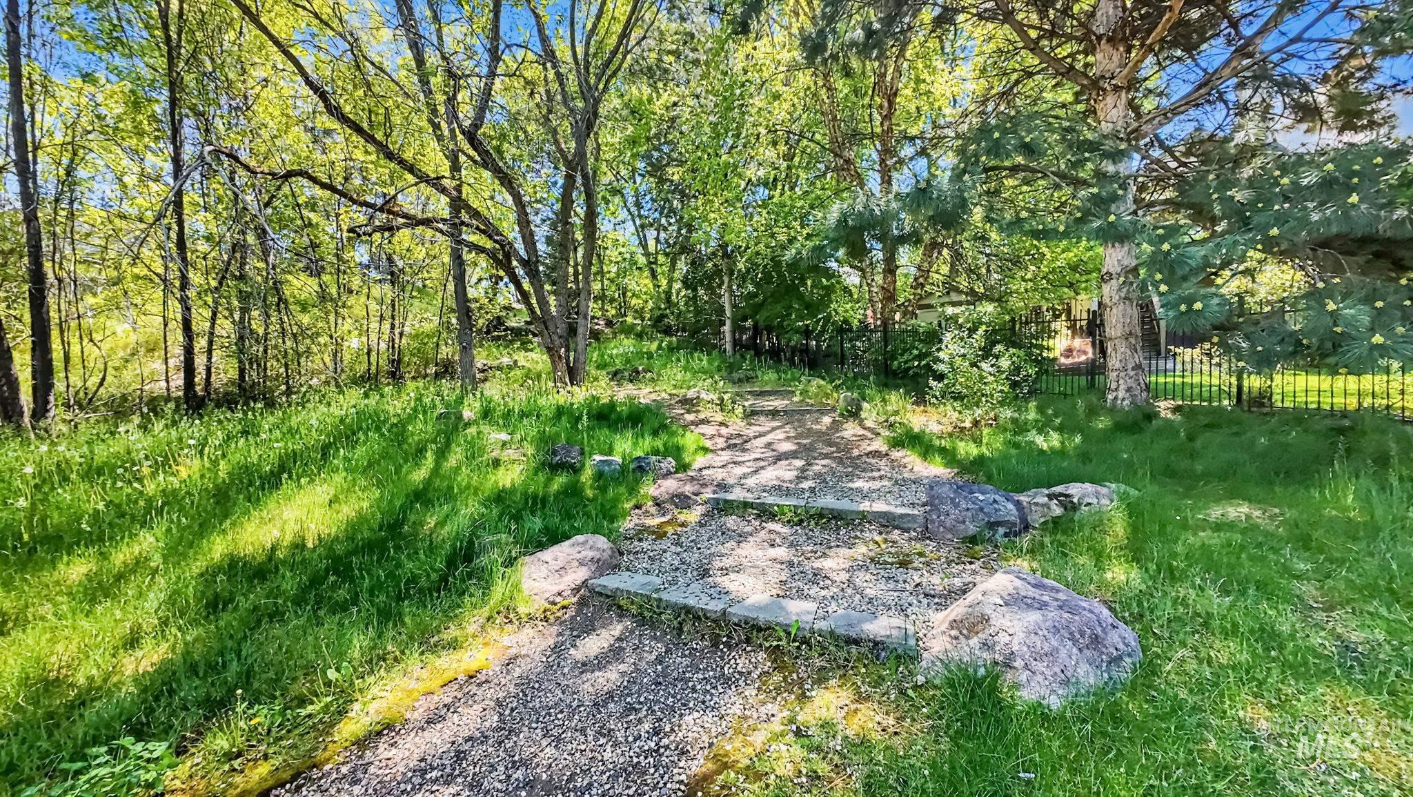 1579 North Watson Way Eagle, ID 83616 - Photo 29 of 30 Landscaped pathway featuring gravel steps, natural boulders, a wrought iron fence, mature trees, and lush green grass