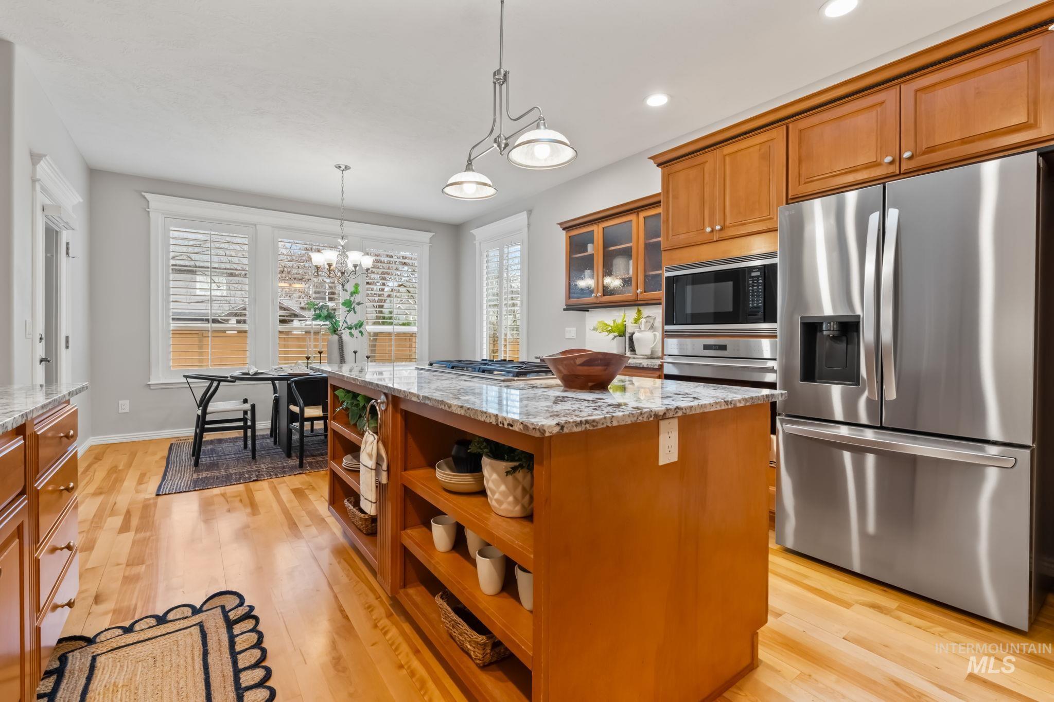 1579 North Watson Way Eagle, ID 83616 - Photo 5 of 30 Kitchen with stainless steel appliances, wood finish cabinetry, a center island, light stone countertops, and light wood-style floors
