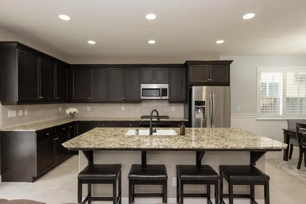 a kitchen with granite countertop a table chairs microwave and refrigerator