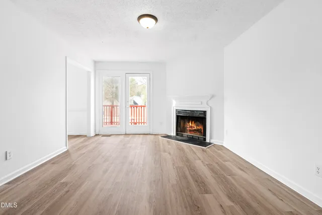 an empty room with wooden floor fireplace and windows