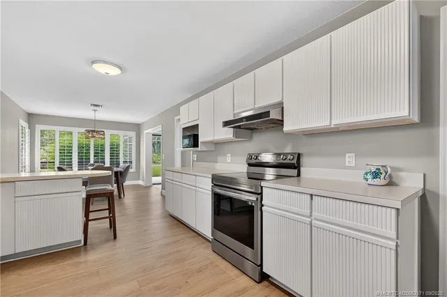 a kitchen with stainless steel appliances granite countertop a stove a sink dishwasher and white cabinets with wooden floor