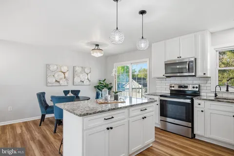 a kitchen with granite countertop stainless steel appliances a stove a sink a microwave a dining table and chairs with wooden floor